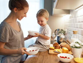 Madre y niño en la cocina, sentado en la mesada con un tazón, queso y pan, alimento energético