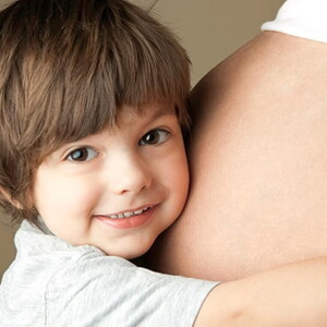 Niño pequeño sonriendo y abrazando el vientre de mamá embarazada.