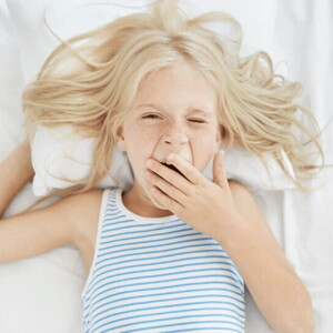 Niña rubia bostezando en la cama con ganas de dormir bien