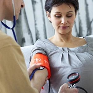 Doctor y mujer embarazada con un tensiómetro en el brazo midiendo su presión alta en el embarazo